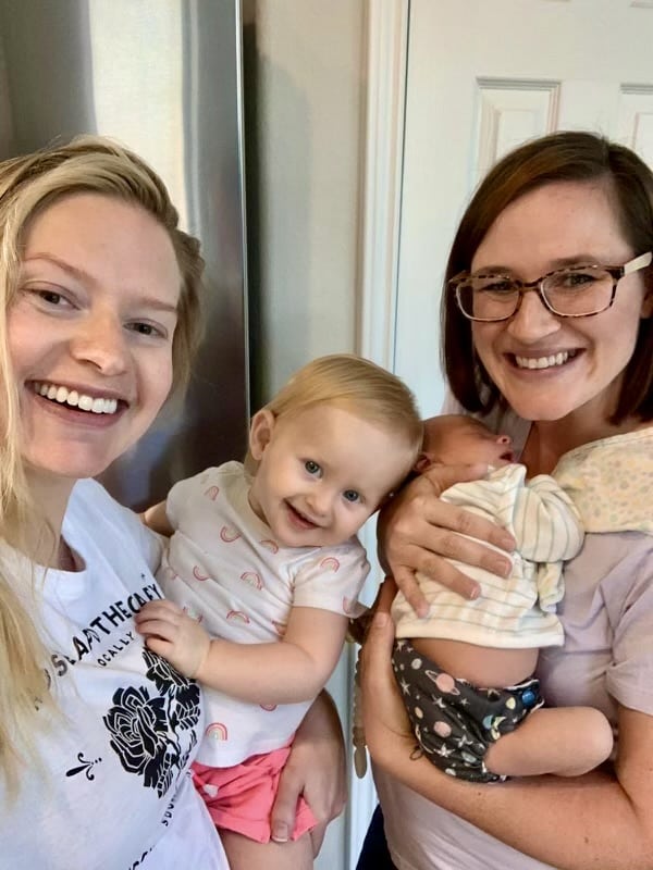 Three women holding babies in a kitchen.