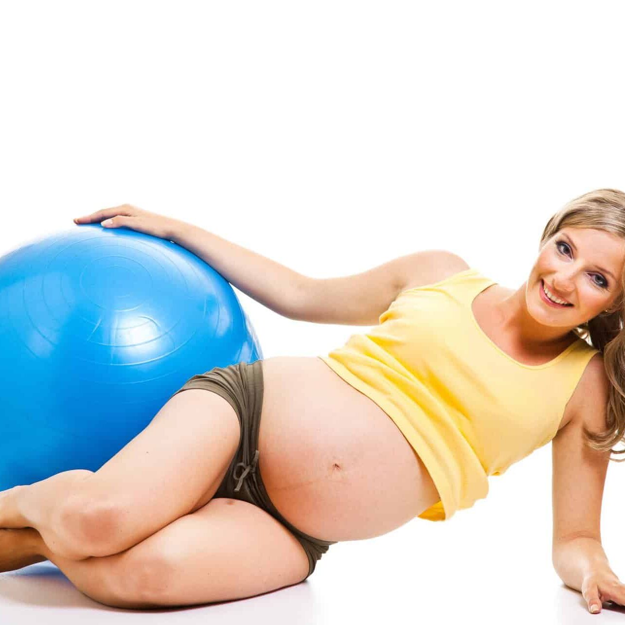 A pregnant woman laying on a blue exercise ball.